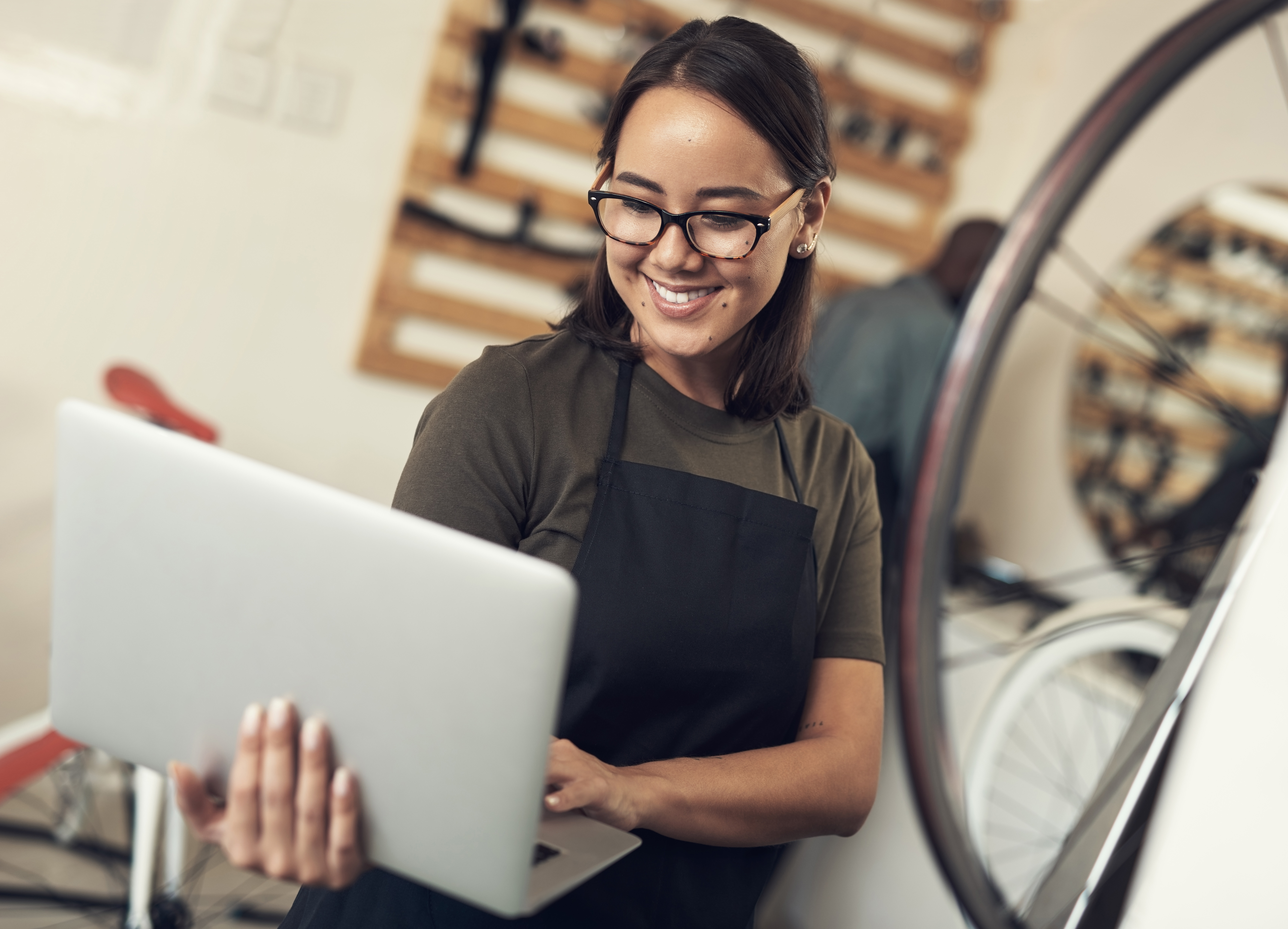 A woman wearing an apron is using a laptop in a bicycle shop